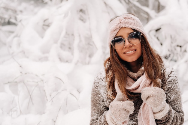 Uma garota com um suéter e óculos no inverno em uma floresta coberta de neve.