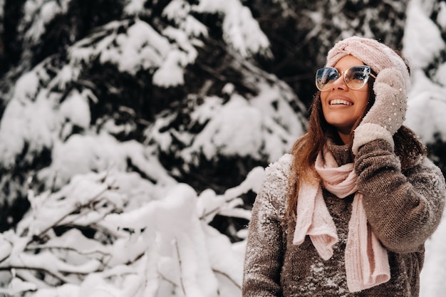 Uma garota com um suéter e óculos no inverno em uma floresta coberta de neve