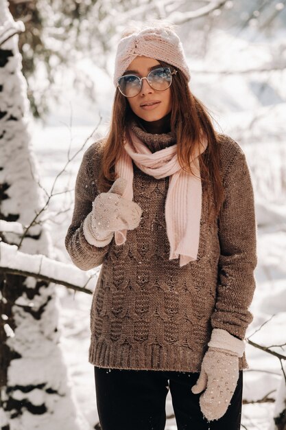 Uma garota com um suéter e óculos no inverno em uma floresta coberta de neve