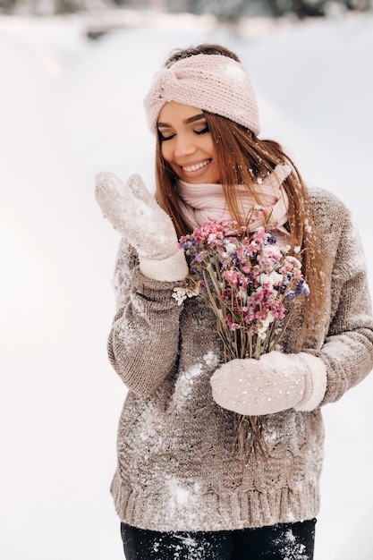 Uma garota com um suéter no inverno com um buquê nas mãos está entre grandes montes de neve