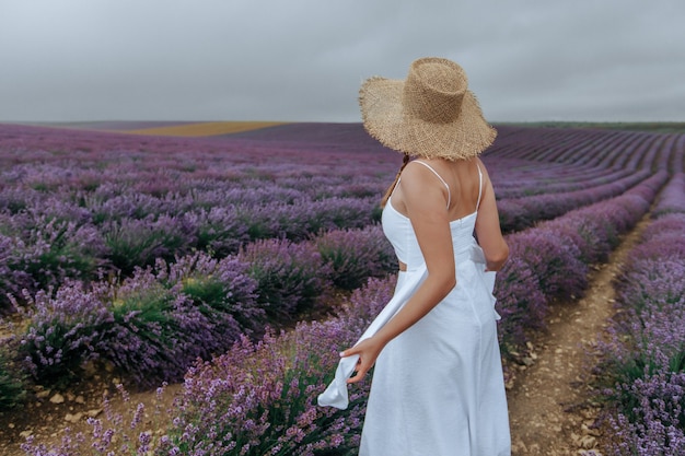 Uma garota com um vestido branco e um chapéu de palha em um campo de lavanda