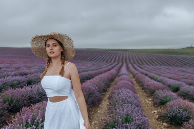 Uma garota com um vestido branco e um chapéu de palha em um campo de lavanda