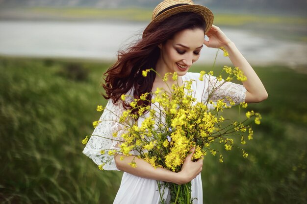 Uma garota com um vestido branco, um chapéu elegante com um buquê de flores amarelas