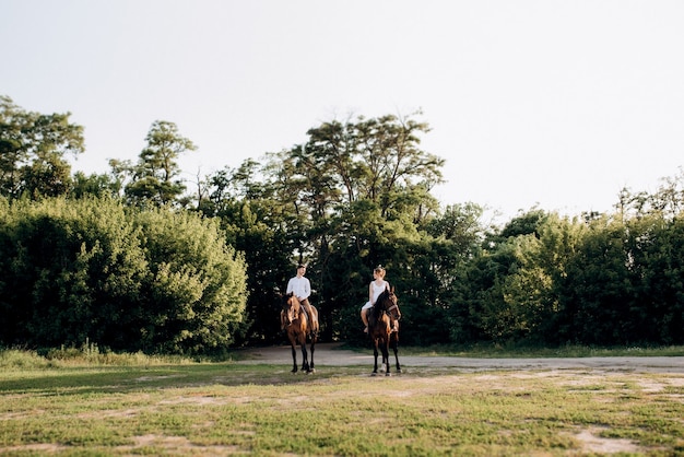 Uma garota com um vestido de verão branco e um cara com uma camisa branca em uma caminhada com cavalos marrons na aldeia