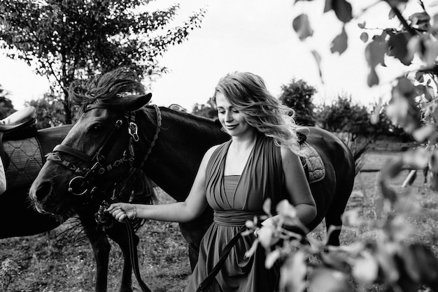 Uma garota com um vestido roxo em uma caminhada com um cavalo. foto em preto e branco.