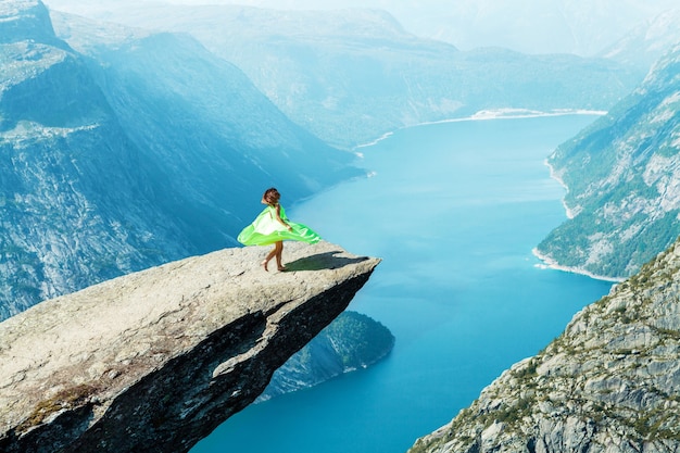 Uma garota com um vestido verde claro dança no trolltunga na noruega