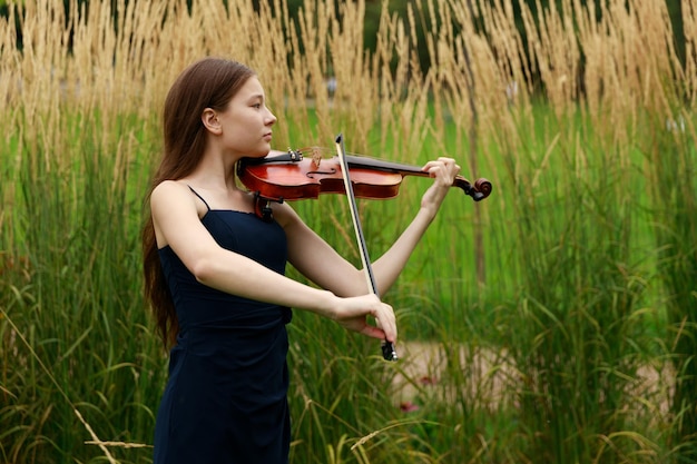 Uma garota com um violino fica no parque no verão