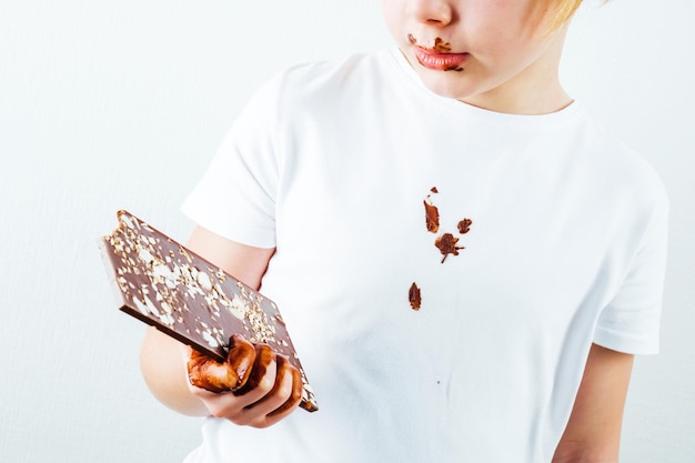 Uma garota com uma camisa branca com chocolate tem uma barra de chocolate na mão.