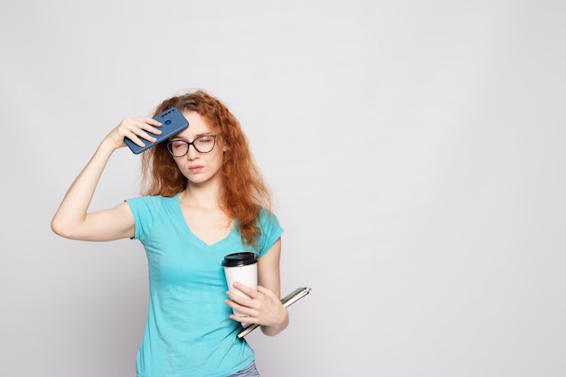 Uma garota com uma camiseta azul com um telefone e café em um fundo claro