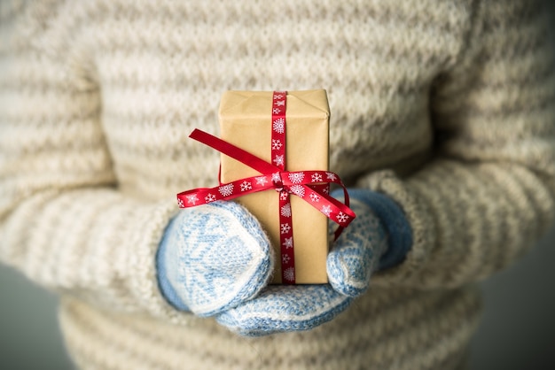 Uma garota com uma camisola de malha quente e luvas está segurando um presente de Natal.