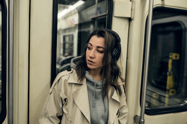 Uma garota com uma capa impermeável bege anda em um vagão do metrô.