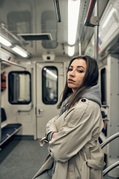 Uma garota com uma capa impermeável bege anda em um vagão do metrô.