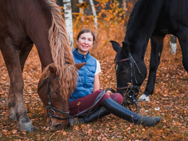 Uma garota com uma jaqueta azul está deitada ao lado do cavalo e ri.