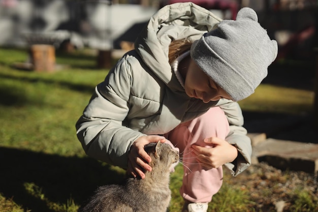 Uma garota com uma jaqueta e chapéu na rua acariciando um gato