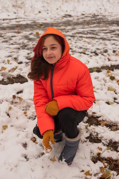 Uma garota com uma jaqueta quente laranja brilhante. Menina com um casaco laranja em tempo de neve. Menina adolescente no inverno