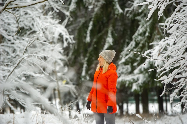 Uma garota com uma jaqueta vermelha caminha por um bosque nevado no inverno.