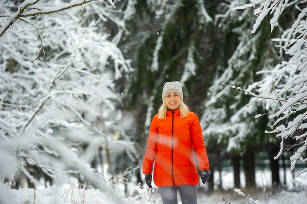 Uma garota com uma jaqueta vermelha caminha por um bosque nevado no inverno.