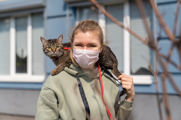 Foto uma garota com uma máscara médica caminha pela rua com um gato