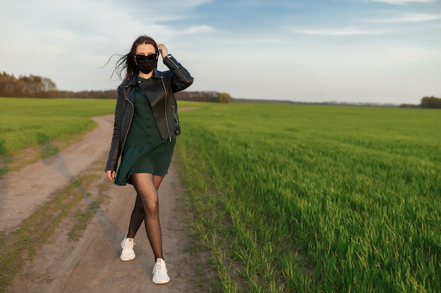 Uma garota com uma máscara médica corre ou caminha em um campo verde. quarentena primavera verão. coronavírus