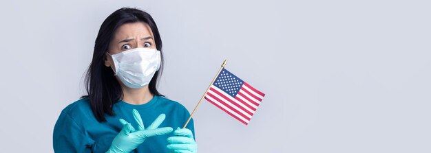 Uma garota com uma máscara médica e luvas segura uma bandeira americana nas mãos. Conceito de Coronavírus