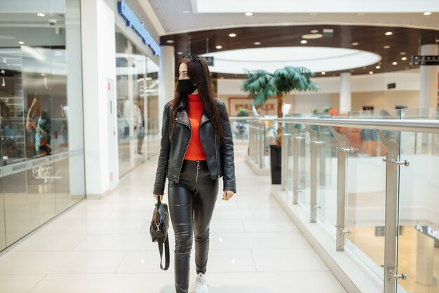 Uma garota com uma máscara médica preta está caminhando em um shopping center.