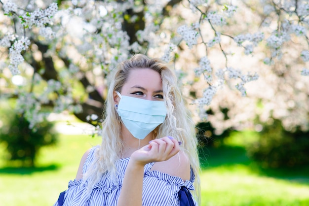 Uma garota com uma máscara médica protetora na primavera entre o jardim florido