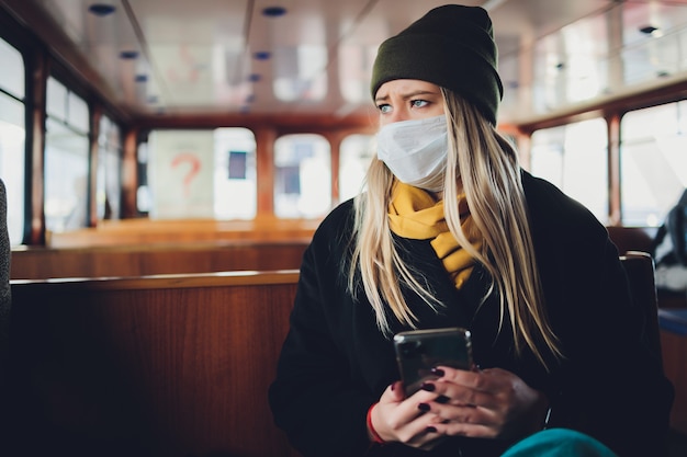 Uma garota com uma máscara protetora em um vagão do metrô com um telefone celular nas mãos