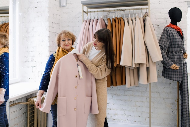 Uma garota consultora em uma loja de roupas ajuda uma cliente idosa a escolher roupas Compras