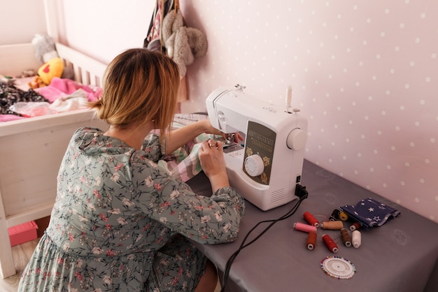 Uma garota costura em uma máquina de costura em casa. A vista traseira é um dos seus hobby favoritos. Produção própria de roupas.