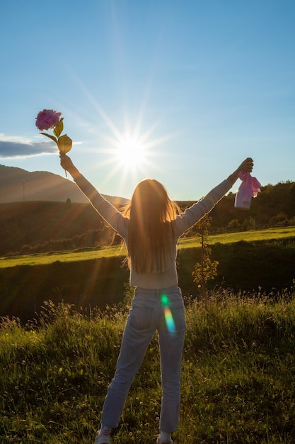 Foto uma garota dá as boas-vindas ao pôr do sol nas montanhas com flores e champanhe