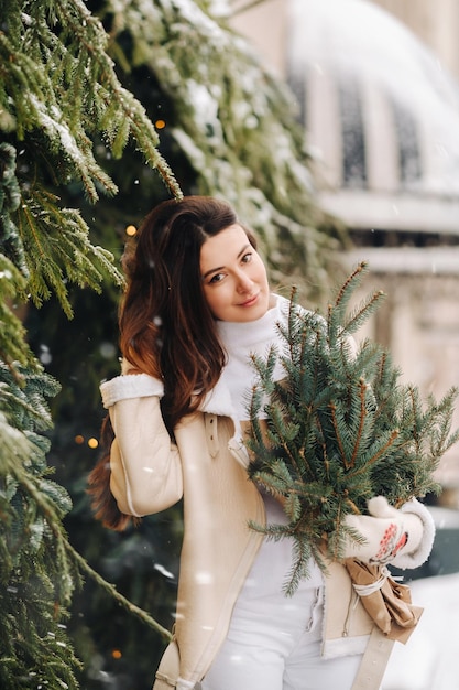 Uma garota de cabelo comprido no inverno na rua com um buquê de ramos de abeto frescos