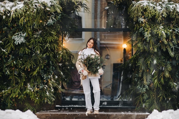 Uma garota de cabelo comprido no inverno na rua com um buquê de ramos de abeto frescos