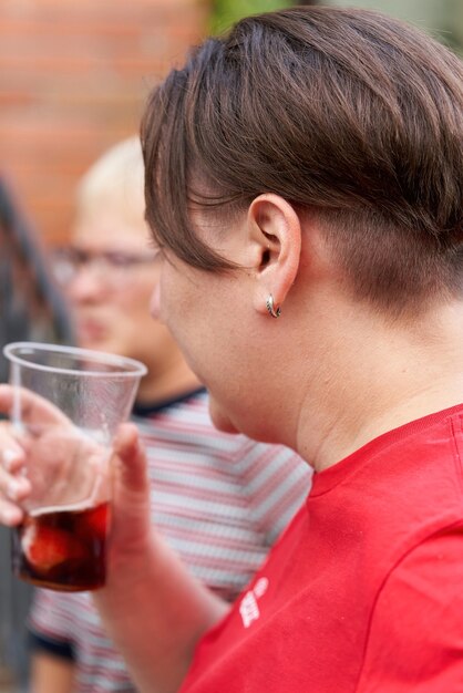 Uma garota de cabelo curto segura um copo descartável de álcool na mão. Vista traseira