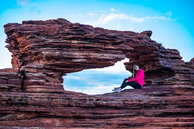 uma garota de cabelos compridos senta-se acima da janela de uma natureza no parque nacional kalbarri, no oeste da austrália