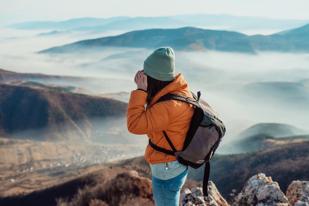 Uma garota de caminhada com uma mochila nas costas observa a manhã do topo da montanha