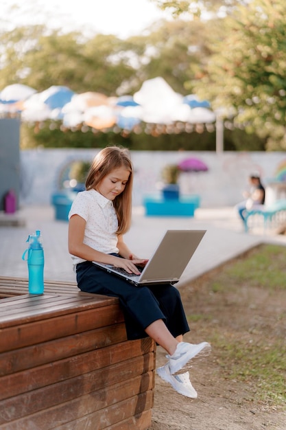 uma garota de camisa e shorts está sentada no parque com um laptop estudando e uma garrafa de água