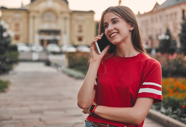 Uma garota de camiseta vermelha falando ao telefone na praça e olhando para longe