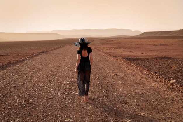 Uma garota de chapéu caminha por uma estrada perto da cidade de Ouarzazate. Marrocos