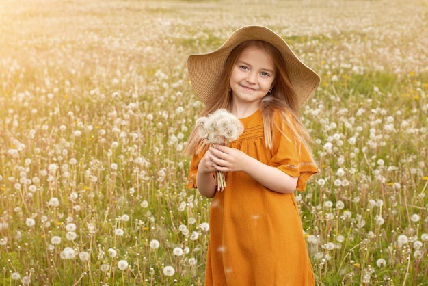 Uma garota de chapéu em um campo com um dente de leão branco uma criança segurando um buquê de flores Copiar espaço