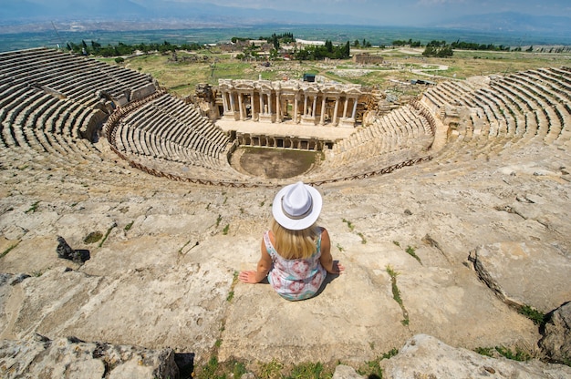 Uma garota de chapéu está sentada em um anfiteatro romano nas ruínas de hierápolis, em pamukkale, turquia.