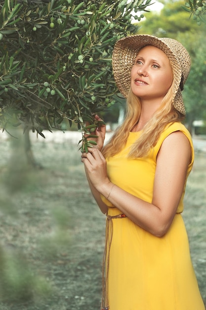 Uma garota de chapéu fica perto de uma oliveira