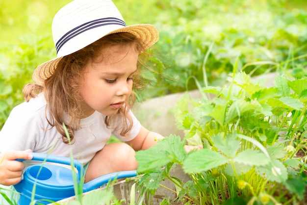 uma garota de chapéu regando uma fileira no jardim de um regador