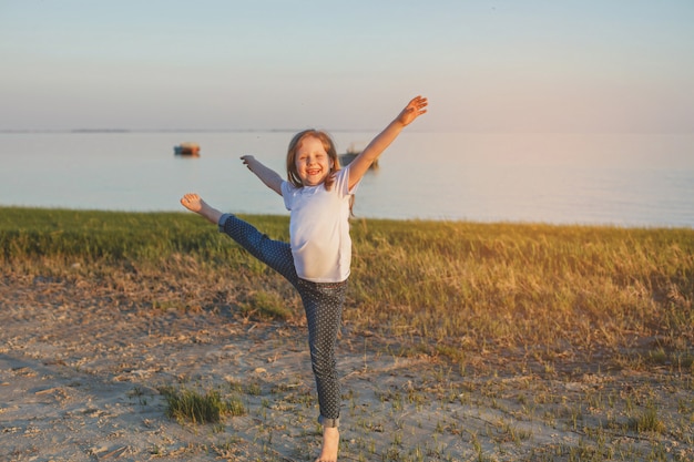 Uma garota de jeans e uma camiseta dançando com os pés descalços na praia no verão