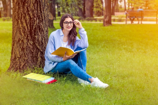 Uma garota de óculos com livros está sentada no parque