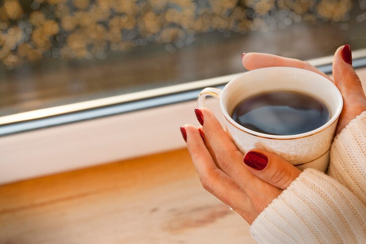 Foto uma garota de suéter está de pé junto à janela com uma xícara de café. fora do brilho da janela, bokeh