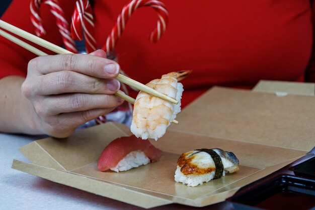 Uma garota de suéter vermelho segura sushi com camarão rei com pauzinhos Frutos do mar