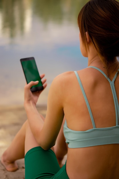 uma garota de uniforme esportivo tem um telefone nas mãos, vestida com uma blusa verde e bicicleta