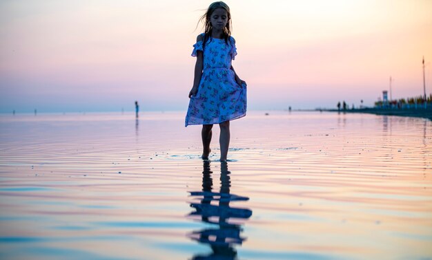 Uma garota de vestido à beira-mar ao pôr do sol caminha sobre a água