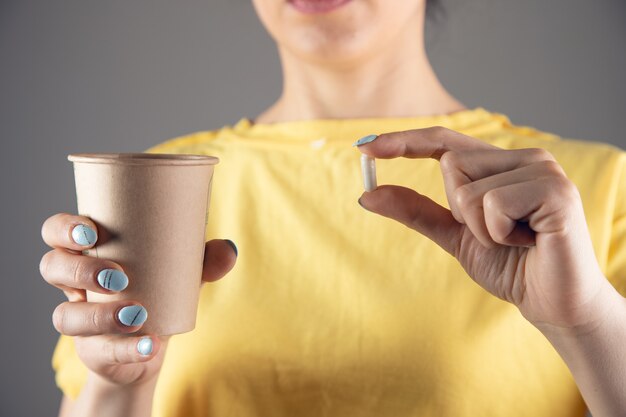 Uma garota de vestido amarelo segurando um comprimido e um copo d'água