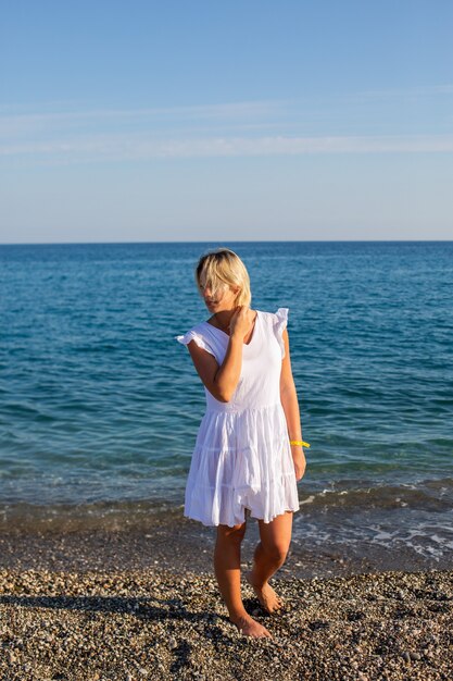 Uma garota de vestido branco caminhando à beira-mar